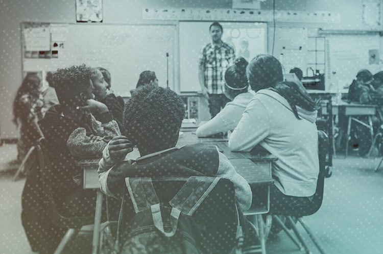 A teacher instructs a group of high school students sitting at desks